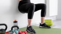 Kvinde med træningstøj laver squat op ad en væg, kun synlig fra talje og ned. 