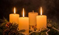 Adventskrans i gran og fire hvide stearinlys hvor tre er tændt, dæmpet stemningsfuld belysning.