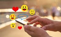 Billede viser et par hænder der holder en smartphone og er ved at klikke, og ovenpå animeret en masse glade smileyer/emojis og hjerter. 