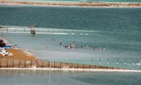 Landskabsbillede viser udsnit af stranden ved Det Døde Hav, hvor psoriasispatienter sendes i klimabehandling. En gruppe mennesker bader i det salte vand ved bredden og flyder. 